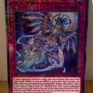 May include: A blue and white card with the text "Dominus Impulse" and "Trap Card" in red. The card features an illustration of a blue and white dragon with a smaller, white figure in front of it. The card is from the Yu-Gi-Oh! Trading Card Game.