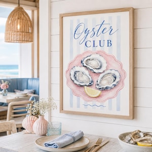 May include: A framed watercolor print featuring the words "Oyster Club" in elegant script. The artwork depicts three oysters on a pink scalloped plate with a lemon wedge, set against a backdrop of blue and white stripes.