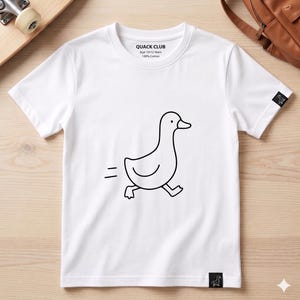 May include: White t-shirt with a black outline drawing of a running duck. The shirt has the text "QUACK CLUB" and "Age 10-12 Years 100% Cotton" printed on the front. A small duck logo is on the sleeve.