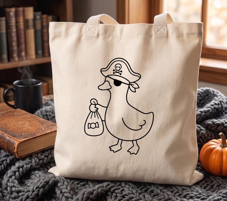 May include: A cream-colored canvas tote bag featuring a black line art illustration of a duck dressed as a pirate. The duck wears a pirate hat with a skull and crossbones symbol and an eye patch, while holding a small sack of candy in its wing.