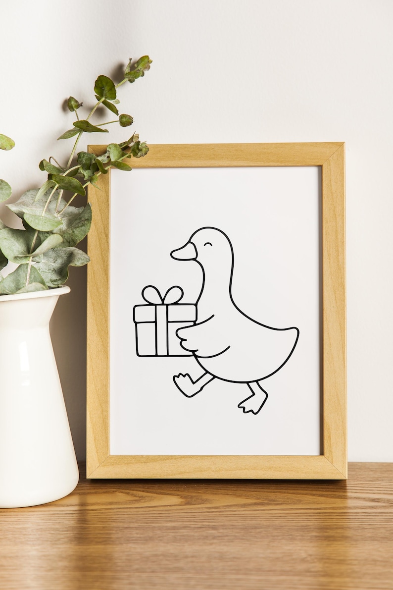 May include: A framed art print featuring a black and white line drawing of a duck carrying a gift box. The duck is smiling and walking, with the gift box held in its wing. The artwork is in a light brown wooden frame.