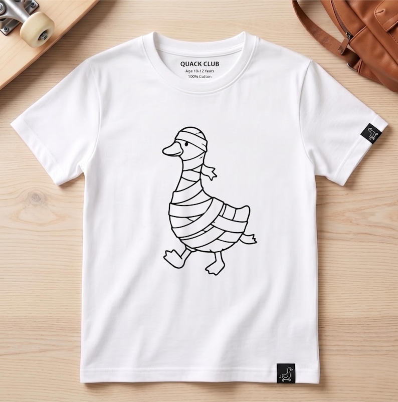 May include: A white short-sleeve t-shirt featuring a black line art graphic of a duck wrapped in bandages like a mummy. The inner neck label reads QUACK CLUB, Age 10-12 Years, 100% Cotton. A small black tag with a duck icon is on the sleeve and hem.