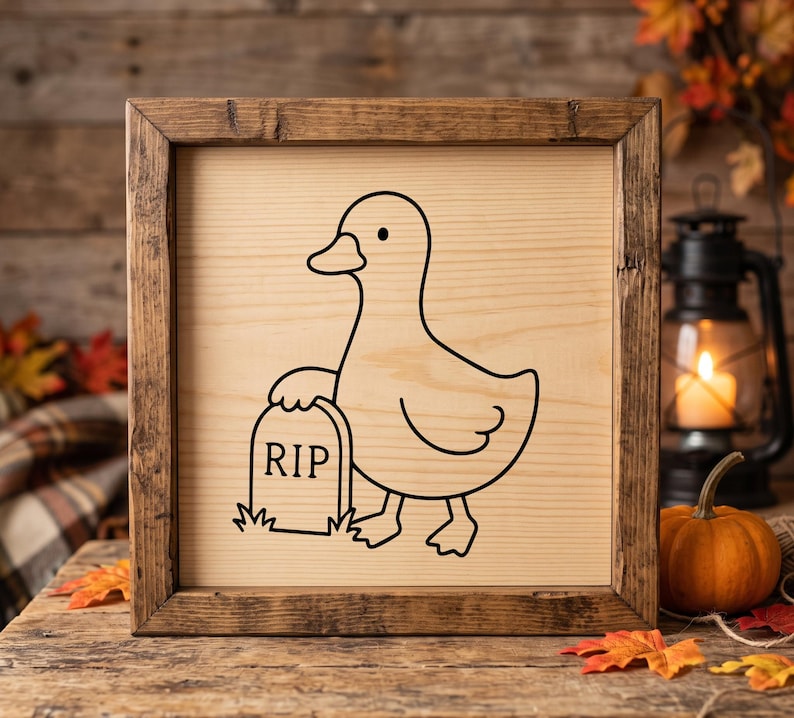 May include: A square wooden sign with a dark brown frame featuring a black line art illustration of a duck standing next to a tombstone with the text RIP engraved on the light-colored wood surface. The design is centered on the flat wooden panel.