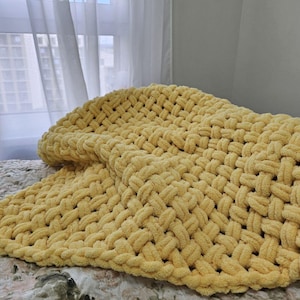 Pu&ograve; includere: Una coperta di lana gialla con una trama a maglia grossa. La coperta &egrave; piegata e drappeggiata su un letto.