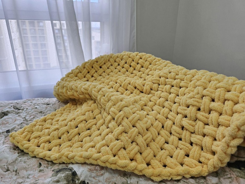Pu&ograve; includere: Una coperta di lana gialla con una trama a maglia grossa. La coperta &egrave; piegata e drappeggiata su un letto.