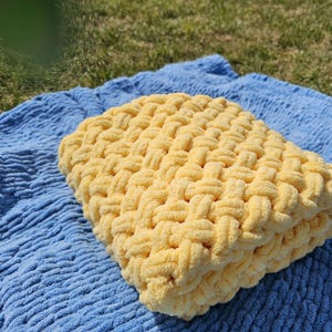 Pu&ograve; includere: Una coperta di lana gialla con un motivo intrecciato, appoggiata su una coperta blu testurizzata.