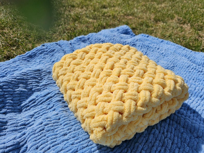 Pu&ograve; includere: Una coperta di lana gialla con un motivo intrecciato, appoggiata su una coperta blu testurizzata.