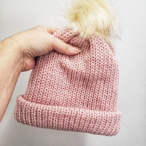 May include: A pink knitted beanie with a fluffy white pom pom on top.