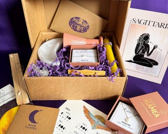 May include: A brown cardboard box filled with a variety of items, including a moonstone necklace, a moon-shaped crystal, a candle, a small pink vase, a wooden stick, and a card with a moon calendar. The box is open and the items are visible. The box is labeled "Moon Love".