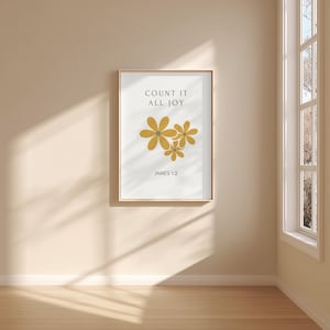 May include: A framed art print featuring the text "COUNT IT ALL JOY" above a cluster of stylized yellow flowers. The text "JAMES 1:2" is below the flowers. The print is in a light-colored wooden frame.