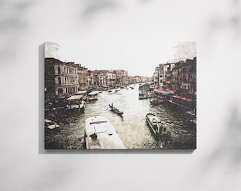 May include: Canvas print of a canal scene in Venice, Italy. The artwork depicts buildings lining the waterway, with boats and gondolas navigating the water. The color palette is muted, with shades of brown, beige, and gray.