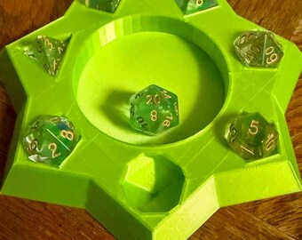 Puede incluir: Una bandeja para dados de color verde lima brillante en forma de estrella con un área central circular para lanzar y seis ranuras empotradas en el perímetro. La bandeja contiene siete dados poliédricos verdes translúcidos con números dorados, incluido un dado de veinte caras en el centro.