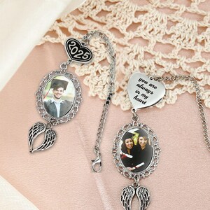 May include: Two graduation-themed car charms. One features a photo in an oval frame with angel wings, a chain, and a charm with the year 2025. The other has a heart charm with the text "you are always in my heart" and a photo in an oval frame with angel wings.