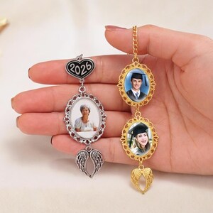 May include: A personalized photo charm with three oval frames. The top frame has the year "2026" on a heart-shaped charm. The other two frames hold photos, with a pair of angel wings at the bottom of each charm. One charm is silver, the other gold.