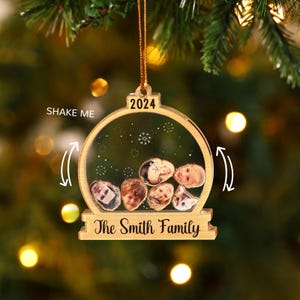 May include: A wooden Christmas ornament with a clear center, featuring family photos and the text "The Smith Family." The ornament is shaped like a snow globe, with the year "2024" at the top and the words "Shake Me" on the side.