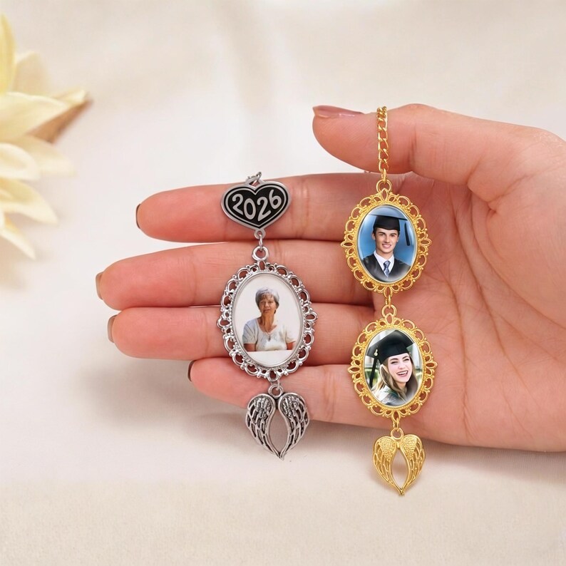 May include: A personalized photo charm with three oval frames. The top frame has the year "2026" on a heart-shaped charm. The other two frames hold photos, with a pair of angel wings at the bottom of each charm. One charm is silver, the other gold.