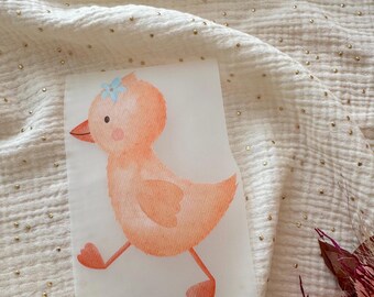May include: A watercolor illustration of a peach-colored duckling with a blue flower on its head. The duckling is walking, with its wings slightly open. The image is on a white background.