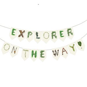 K&ouml;nnte beinhalten: Eine Girlande mit cremefarbenen Wimpeln, die das Wort "EXPLORER ON THE WAY" bilden. Die Buchstaben sind mit nat&uuml;rlichen Elementen wie Bl&auml;ttern und Zweigen verziert, was ein rustikales, von der Natur inspiriertes Design ergibt.