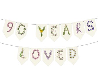 Pode incluir: Uma faixa com as palavras "90 YEARS LOVED" em bandeirolas creme. As letras e números são decorados com várias flores e vegetação, criando um design floral para uma celebração.