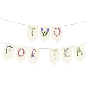 A floral banner with the words 'Two for Tea' spelled out using wildfowers. The O is with pink obedient flowers, the L with licorice flowers, I with sage, V with purple violets, R with redbuds and Y with yellow yarrow. The banner is made of a very light cream paper and there is a string running through the top. The letters are on individual rectangular papers with pointed tips. It has a rustic, cottage garden boho vibe.