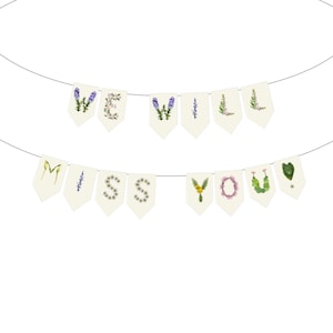 May include: A banner with the words "WE WILL MISS YOU" spelled out on individual cream-colored pennants. The letters are decorated with various flowers and greenery, creating a floral design.