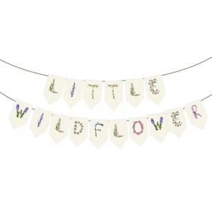 May include: A banner with the words "WILD FLOWERS" and "LITTLE" spelled out on cream-colored pennants. Each letter is decorated with floral designs in shades of purple, green, and pink. The banner is strung on a thin green string.