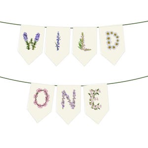 May include: A banner with the words "WILD ONE" spelled out on cream-colored pennants. Each letter is formed with floral arrangements in shades of purple, pink, and white, strung on a green string.
