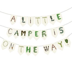 K&ouml;nnte beinhalten: Ein Banner mit drei Reihen von Wimpeln. Die oberste Reihe lautet "A LITTLE". Die mittlere Reihe lautet "CAMPER IS". Die untere Reihe lautet "ON THE WAY". Die Buchstaben bestehen aus nat&uuml;rlichen Elementen.