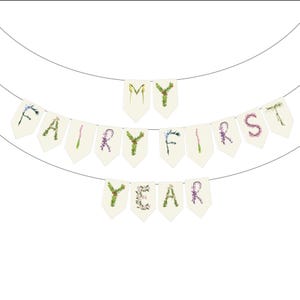 May include: A banner with the words "MY FAIRY FIRST YEAR" spelled out on individual pennants. The letters are decorated with floral and botanical elements, strung on a thin wire against a white background.