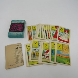 May include: A deck of Old Gypsy Fortune Telling cards with a blue box featuring pink text. The set includes a tan instruction booklet and multiple rectangular cards displaying numbered illustrations, including The Sun, The Scythe, and The Queen.