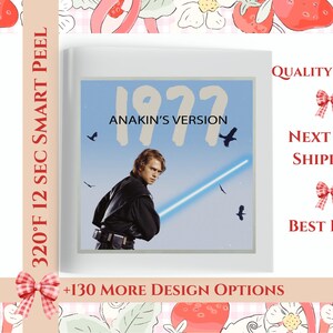 May include: A white square sticker with a blue background and a graphic of a character from Star Wars. The text "1977 ANAKIN'S VERSION" is printed on the sticker.