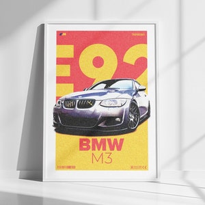 Puede incluir: Un póster enmarcado en blanco con fondo amarillo y rojo que presenta un coche BMW M3 plateado con el texto "E92 BMW M3" impreso en el póster.