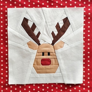 Op de afbeelding: Witte stoffen rendier applique met bruine geweien en een rode neus. Het rendier is op een rode achtergrond met witte sterren.