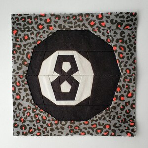 May include: A black and white geometric quilt block with a leopard print border. The block is made up of a series of triangles and squares, creating a complex and interesting pattern.