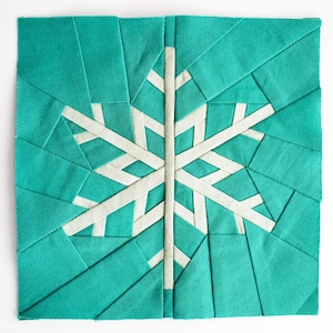 Puede incluir: Un bloque de tela cuadrado, de color turquesa, con un diseño de copo de nieve blanco. El copo de nieve está construido con tiras de tela blanca, y el fondo turquesa está formado por secciones de tela en ángulo. El diseño está centrado sobre un fondo blanco.
