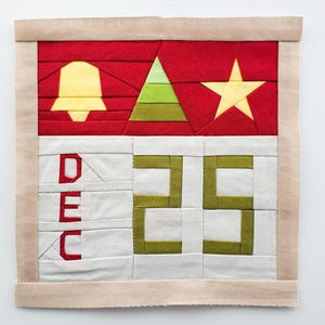May include: A white fabric square with a red, green, and yellow star, bell, and tree design. The square also has the text "DEC 25" in green.