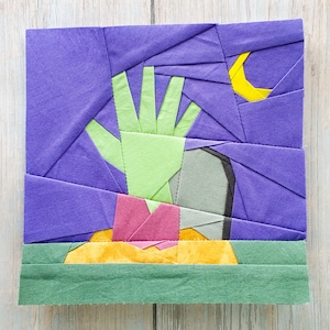 Puede incluir: Una obra de arte textil que representa una mano que emerge de una tumba bajo un cielo púrpura y una luna creciente amarilla. La mano es verde claro, la tumba es gris y el suelo es amarillo y rosa.