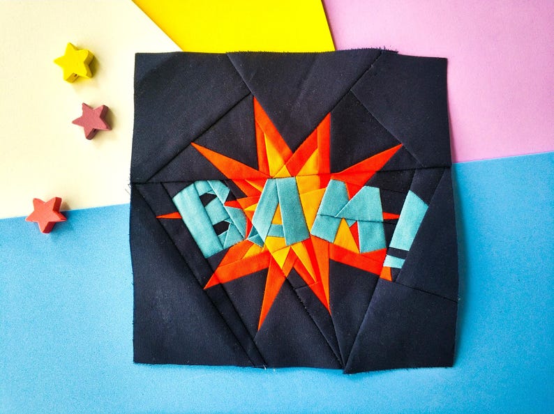 May include: A black fabric square with a red and orange starburst design. The starburst has the word "BAM!" written in blue letters.