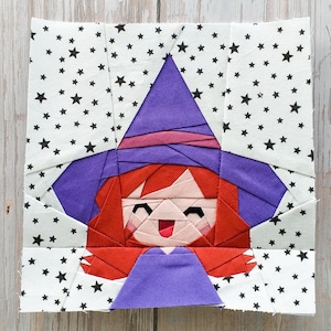 May include: A fabric block featuring a smiling witch with red hair, a purple hat, and a purple dress. The background is white with black stars. The witch is made of various fabric pieces.
