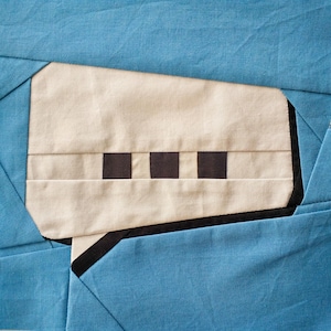 May include: A beige fabric speech bubble with a black border and five black squares in a row across the center. The speech bubble is sewn onto a blue fabric background.
