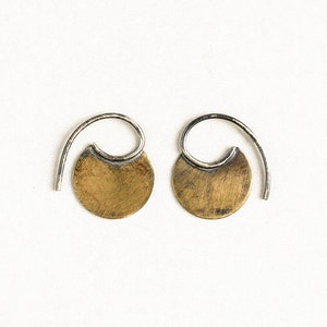 May include: A pair of silver hoop earrings with a gold disc attached to each hoop. The discs have a textured surface.