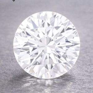 May include: A perfectly round, brilliant-cut diamond, showcasing numerous facets that catch the light. The diamond is set against a grey backdrop. The image includes the text "DIARAYS INC. HOUSE OF LUXURY".