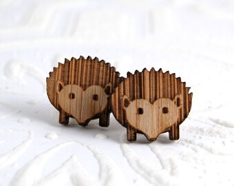 May include: A pair of wooden earrings shaped like hedgehogs. The earrings are brown and have a heart-shaped face.