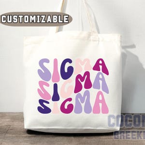 May include: White canvas tote bag with the word "SIGMA" repeated three times in a colorful, retro font. The letters are in shades of pink, purple, and blue.
