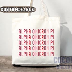 May include: White tote bag with the text "ALPHA OMICRON PI" repeated five times in pink and red lettering.