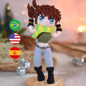 Puede incluir: Muñeca amigurumi de crochet con cabello castaño, camisa verde, pantalones vaqueros azules y botas negras. La muñeca está de pie sobre una base de madera. La muñeca lleva una bufanda verde y amarilla. La muñeca tiene ojos azules y una expresión decidida.
