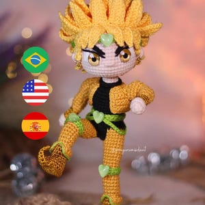 Op de afbeelding: Een gehaakte amigurumi-pop van een personage met geel haar, een groen hart op hun voorhoofd en een gele en groene outfit. De pop staat met één been omhoog en draagt gele schoenen met groene accenten. De pop staat voor drie vlaggen: Brazilië, de Verenigde Staten en Spanje.
