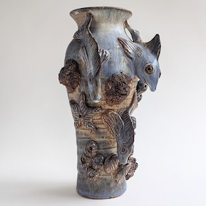 Puede incluir: Un jarrón de cerámica azul y marrón con una superficie texturizada y diseños de peces y corales esculpidos.