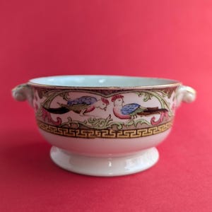 May include: A white porcelain bowl with two handles, featuring a colorful floral design with birds. The bowl has a gold rim and a decorative border.