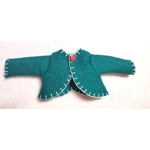 May include: A teal felt jacket with long sleeves and a round neckline. The jacket is hand-stitched with white thread along the edges and features a small red flower button closure. The jacket is designed for a doll.